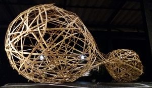 Two connected spherical forms made from split bamboo strips, woven in a random gridshell pattern. Sculptural installation photographed at night.